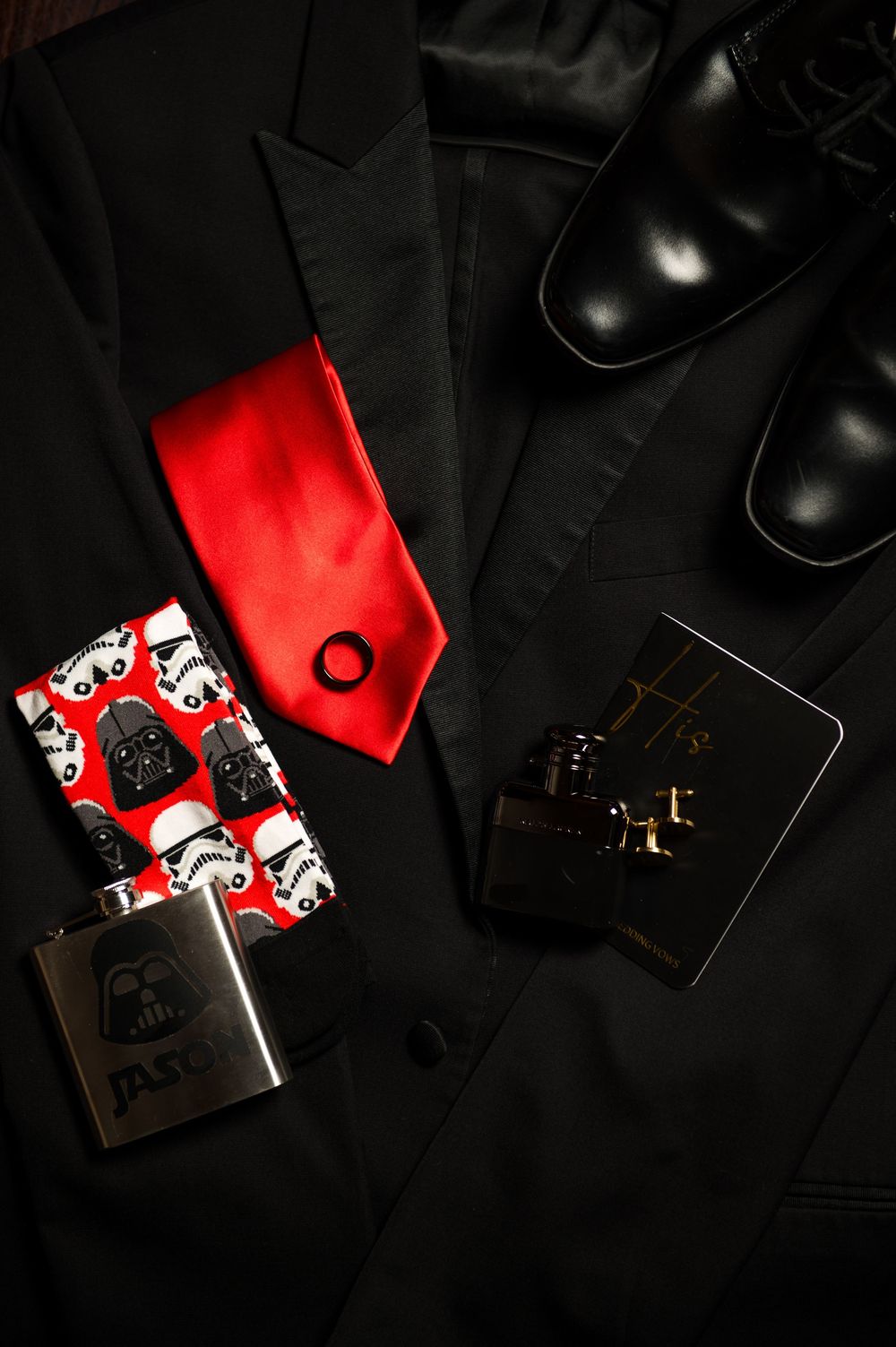 Black suit jacket with red tie and Star Wars themed accessories laid flat on dark surface.