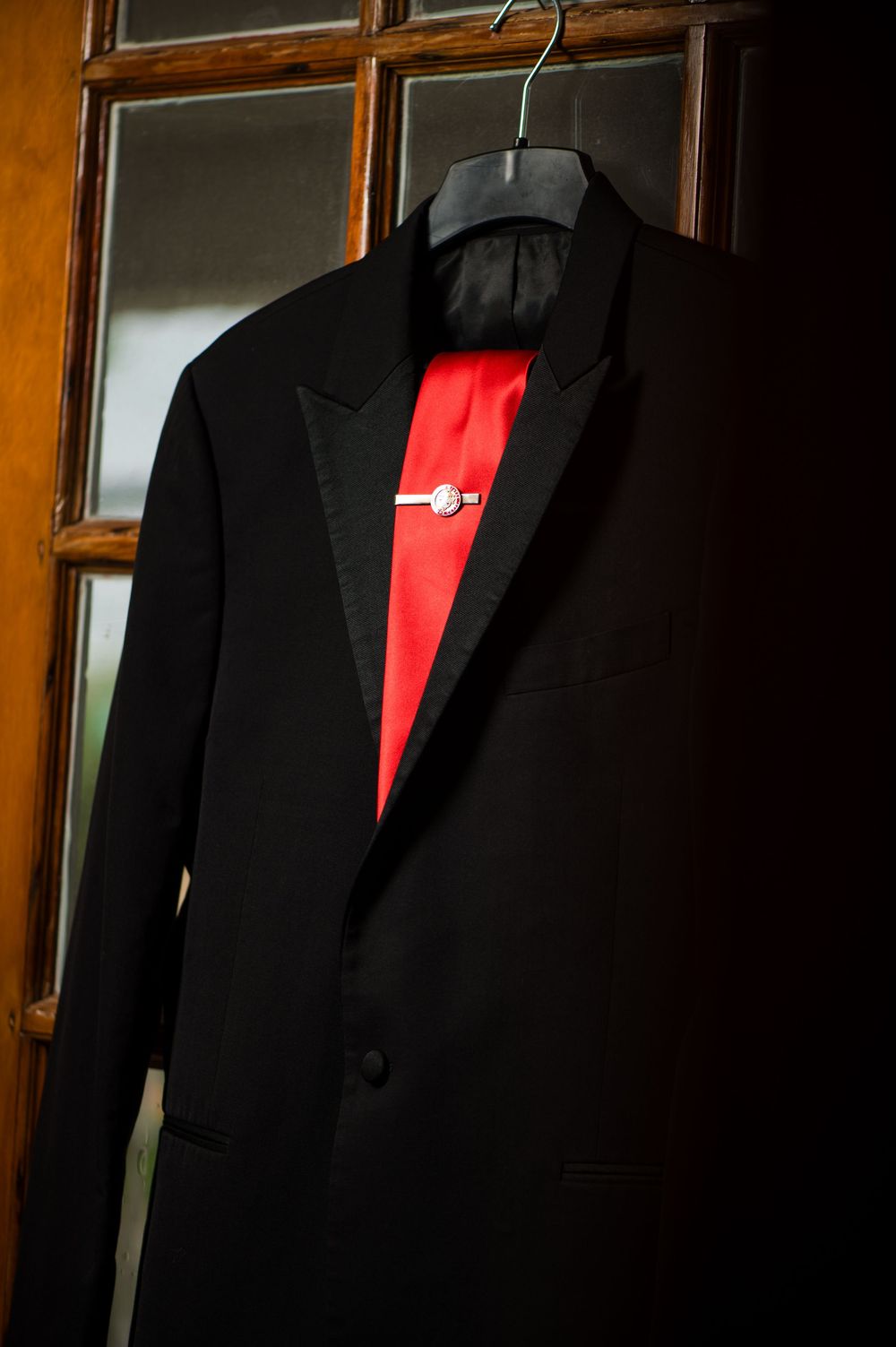 Black suit jackets with red accents hanging in a wooden wardrobe.