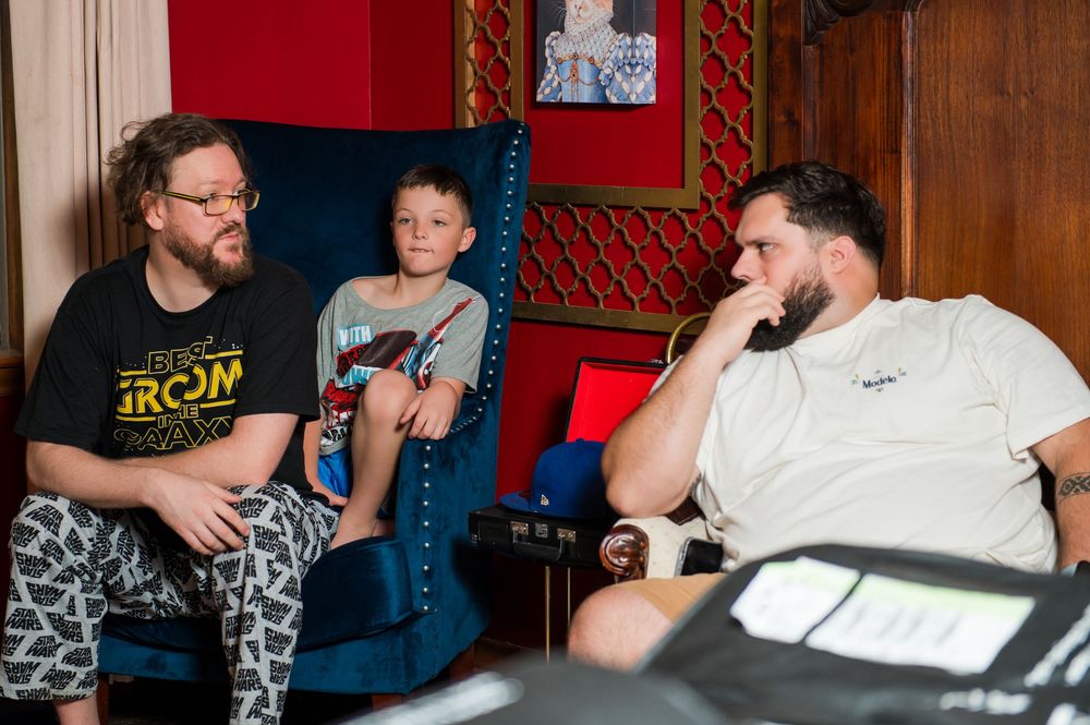 Three people having a casual conversation while seated in a room with red walls.