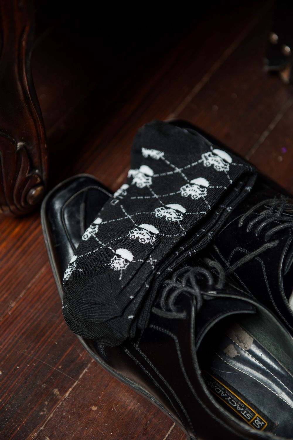 Black suede sneakers with white logo details on wooden flooring.
