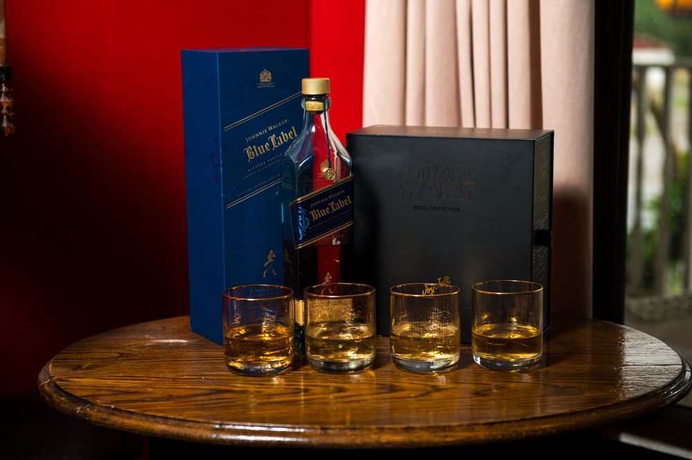 Blue Label whiskey bottle and glasses arranged on wooden table with gift boxes.