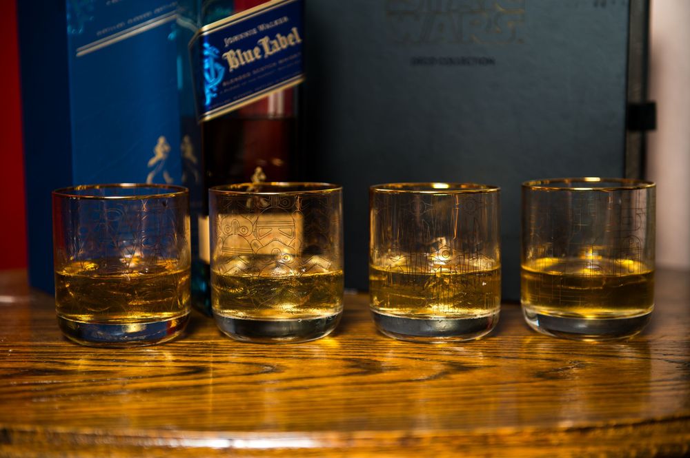 Four glasses of whiskey lined up on a wooden table with amber liquid.
