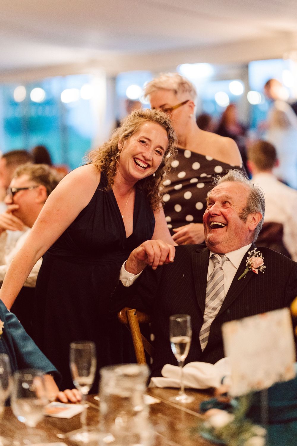 Two guests share a joyful laugh together at an elegant dinner reception with formal attire and table settings.