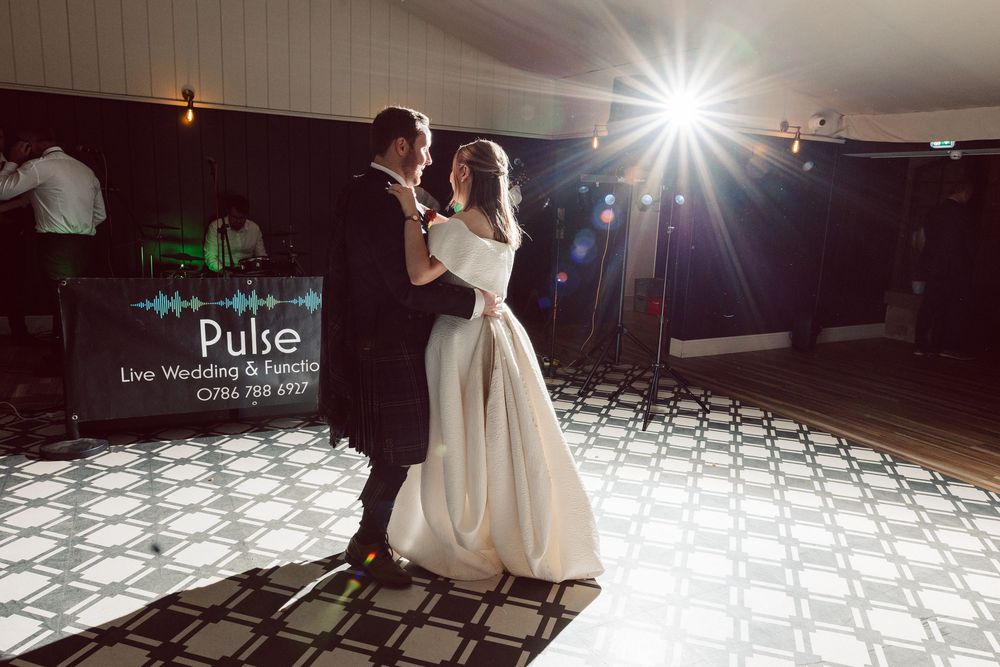 A wedding couple dances on an illuminated LED dance floor while guests watch from the sides during their reception celebration.