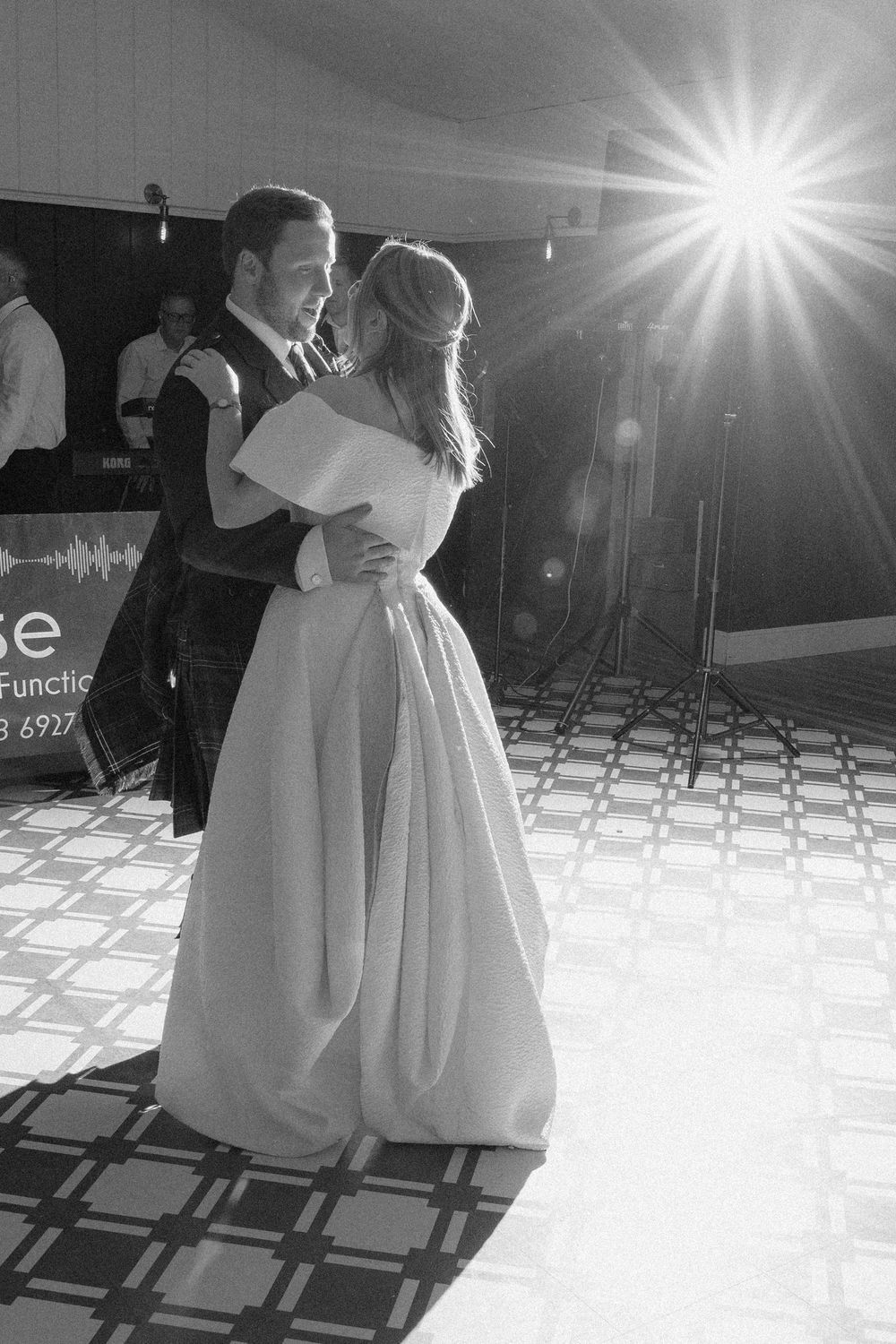 A couple shares their first dance at a wedding reception with dramatic lighting and a checkered dance floor.