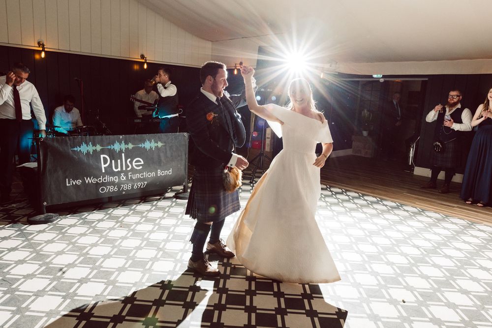 Couples dancing on a checkered floor at an elegant reception venue with dramatic lighting and a romantic atmosphere.