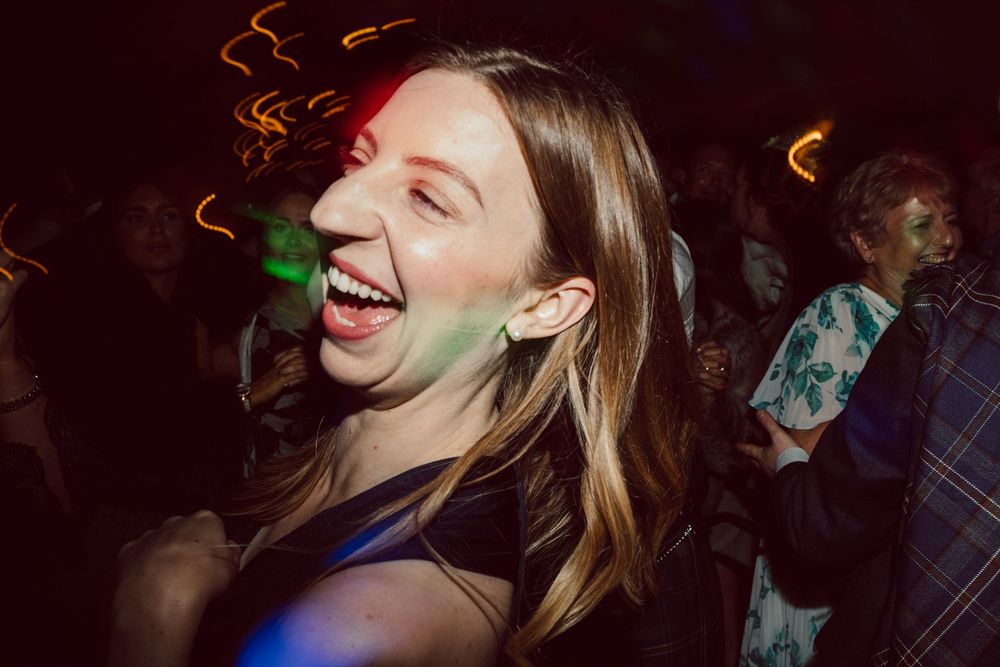 People dancing and laughing at a nightclub party with colorful lights in a dark atmosphere.