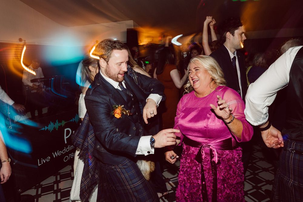 People dancing energetically at a lively wedding reception with colorful lighting and festive atmosphere.