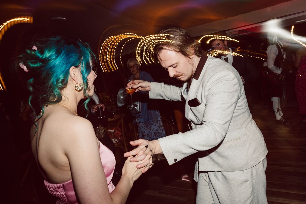 A couple performs a dramatic dance move with a dip on a dark dance floor with other dancers in the background.