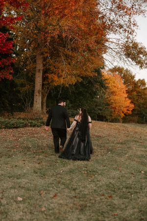 A couple in formal wear walks together on a hill during autumn.
