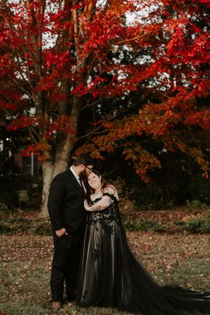 A couple shares an intimate moment in black formal wear beneath bright red fall foliage.