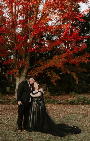 A romantic autumn photoshoot featuring a couple in black formal attire under vibrant red leaves.
