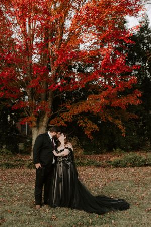 A couple shares a close embrace under a canopy of bright red autumn foliage.