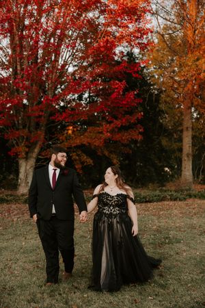 A romantic photoshoot in a park with fall colors featuring a couple in elegant black formal wear.