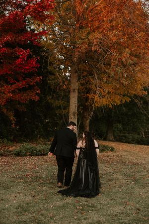 A romantic scene unfolds on a grassy slope with autumn trees creating a colorful natural backdrop.