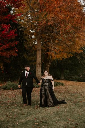 A couple shares a tender moment on a grassy hillside surrounded by autumn trees.