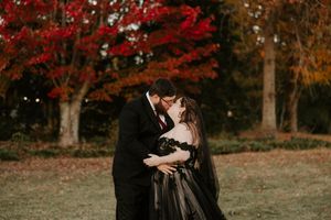 A couple dances together on a hill surrounded by trees with brilliant autumn colors.
