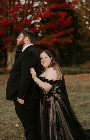 A couple laughs together outdoors wearing black formal attire with stunning fall colors in the background.