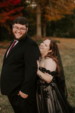 A couple in formal attire shares a romantic moment against vibrant autumn foliage.