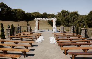 Wooden benches arranged in rows for an outdoor ceremony with white floral arch.