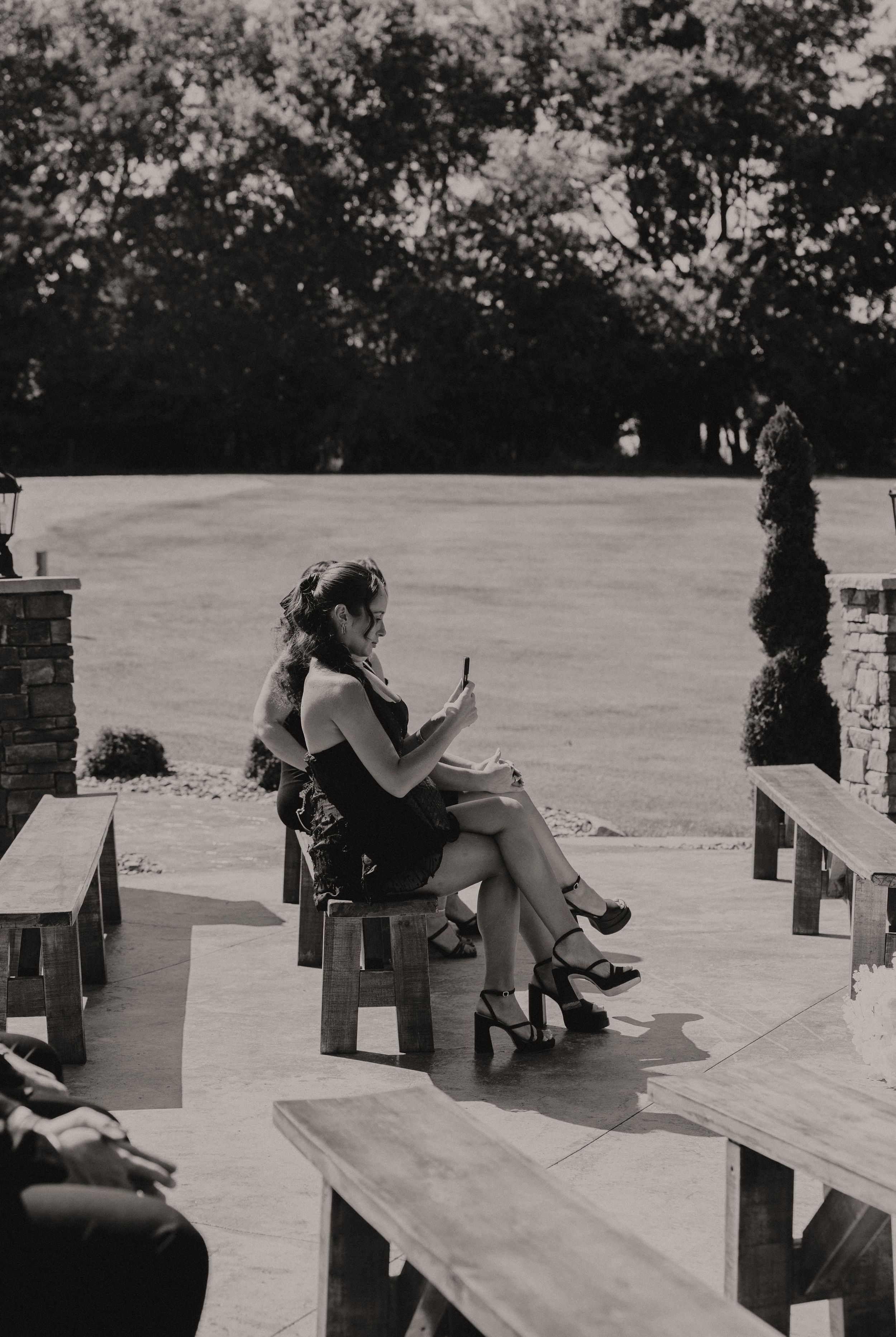 Wedding guests seated on wooden benches during outdoor ceremony.