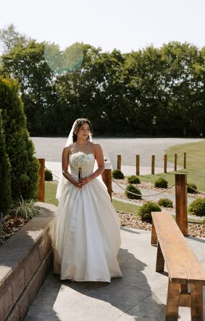 Bride in flowing white ballgown poses on wooden benches in an outdoor venue.