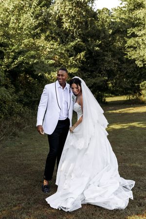 A full-length wedding portrait showing the dramatic train of a white wedding gown in an outdoor setting.