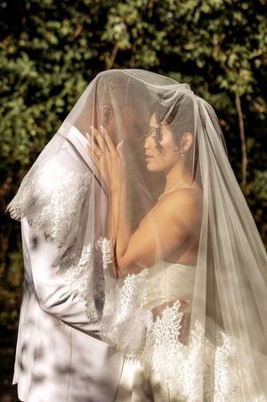 Sunlit outdoor bridal portraits showing detailed lace veil against natural foliage.