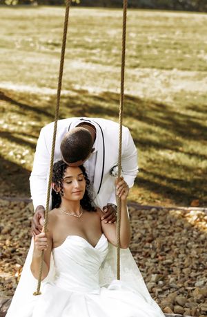 Bride in a white wedding dress poses gracefully on a wooden swing in golden sunlight.