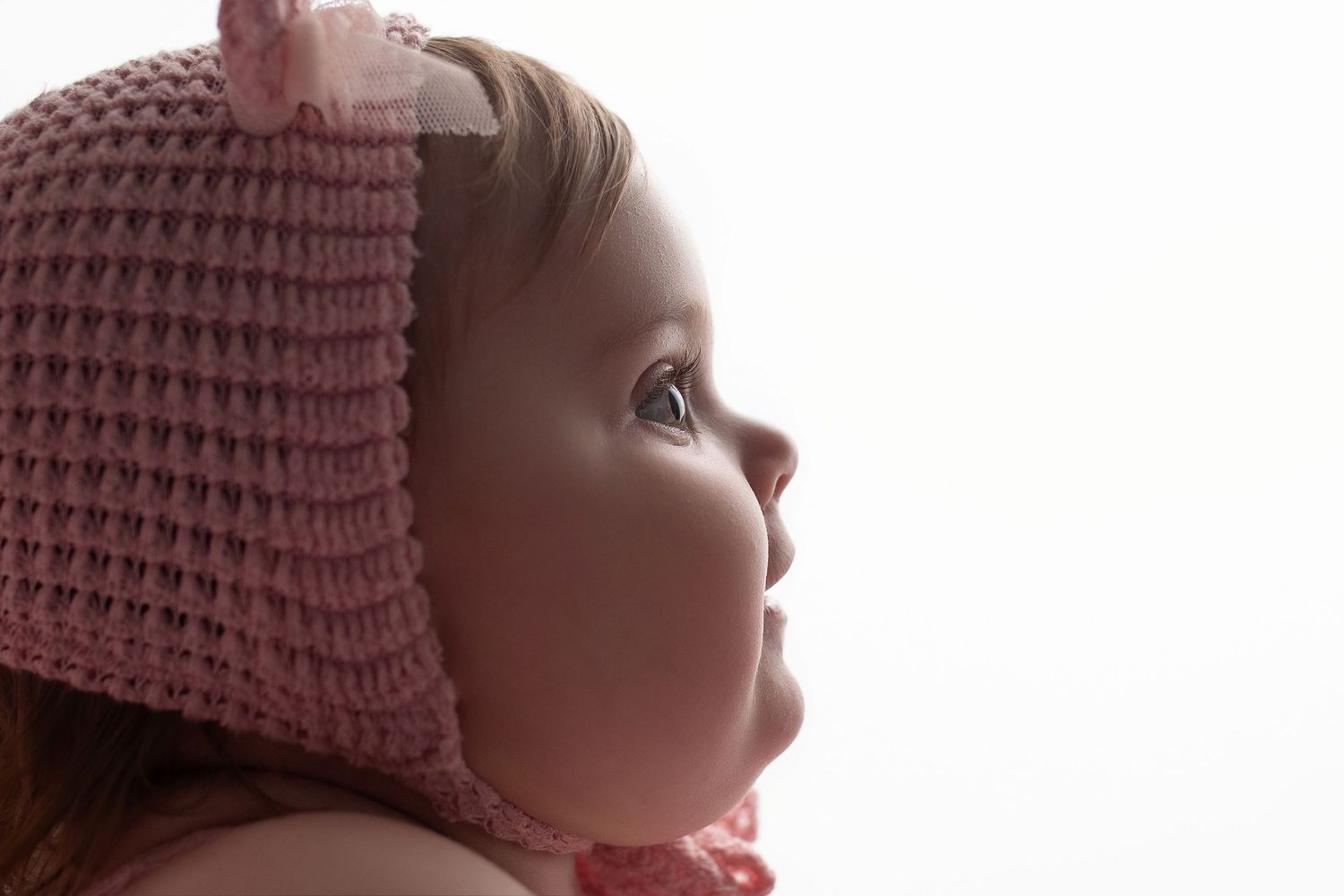 Baby wearing a pink knitted bonnet looks up with wonder in a series of connected profile shots.