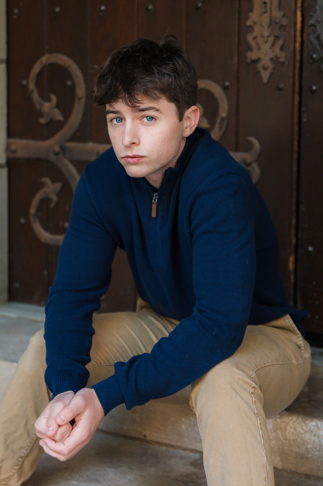 Man sits by door for senior photos taken in Ann Arbor on University of Michigan's campus.