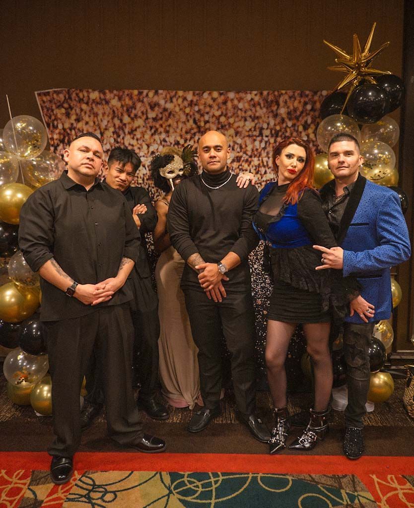 Group of five posing formally before gold and black balloon backdrop with star decoration at gala.