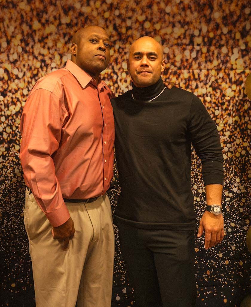 Two men posing together in front of a golden bokeh photo backdrop at a formal event.