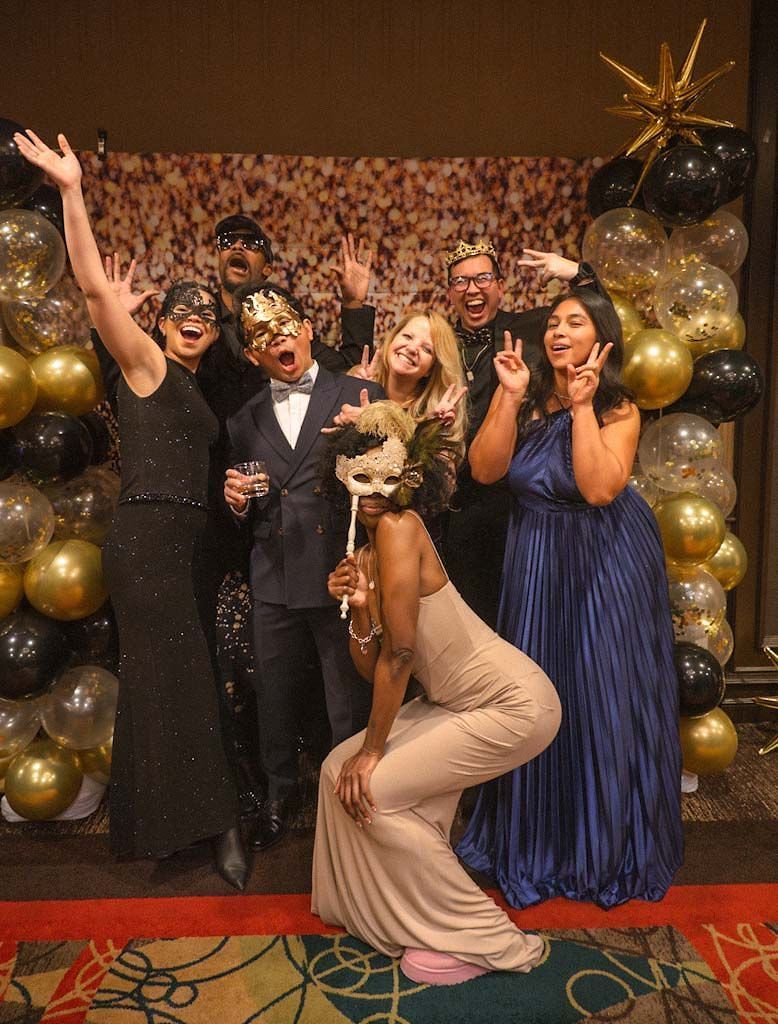 Five guests in formal wear strike fun poses with masquerade masks at a New Year gala.