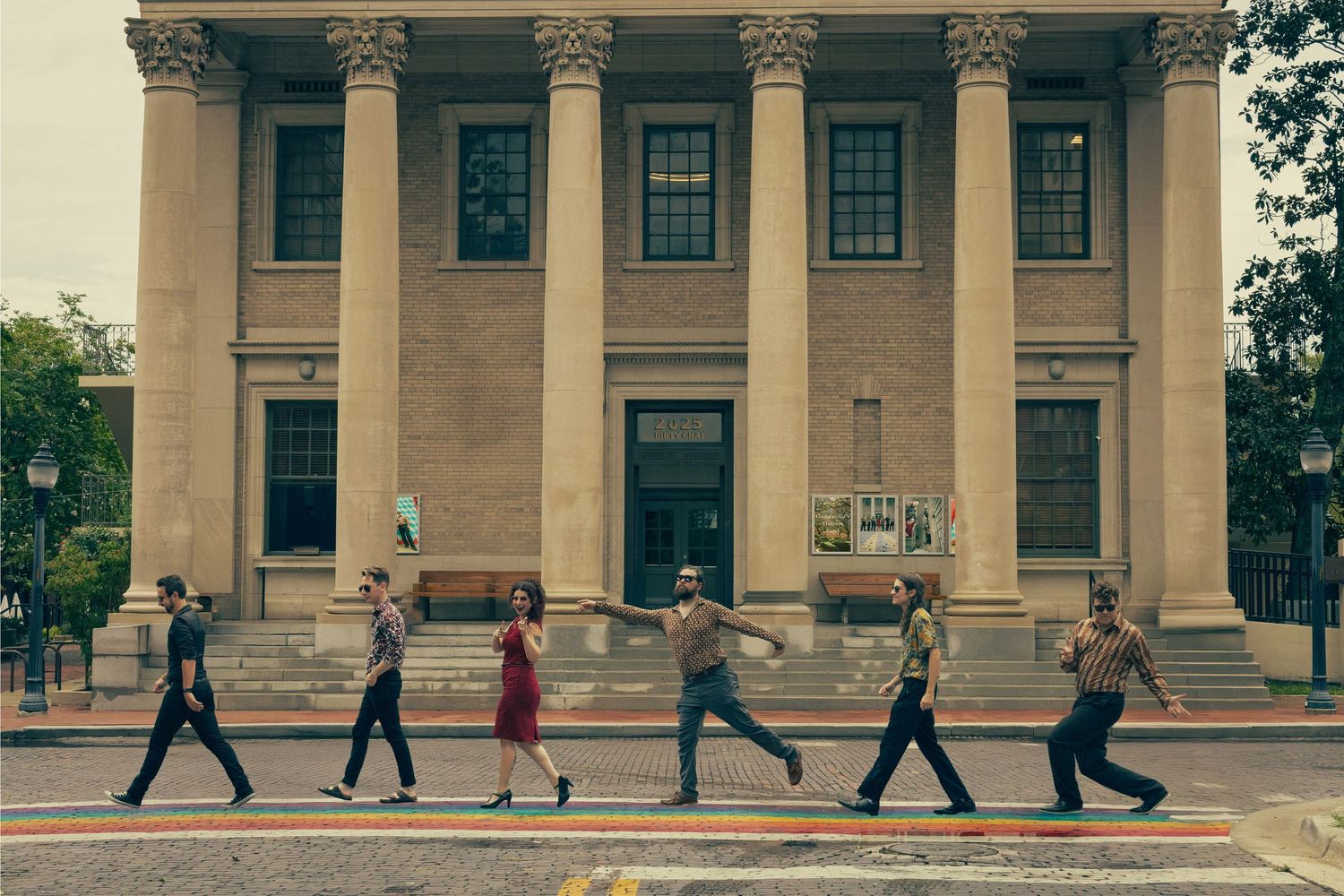 Group of people walking in a line across a crosswalk in front of a classic columned building.