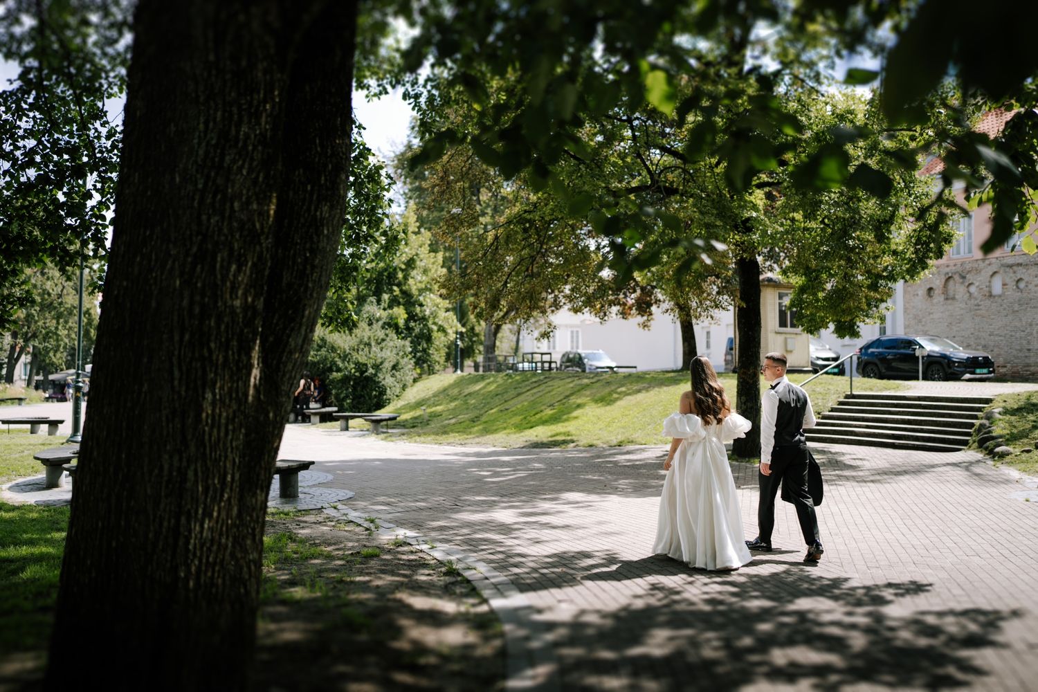 Wedding couple walks along tree-lined path on sunny afternoon.