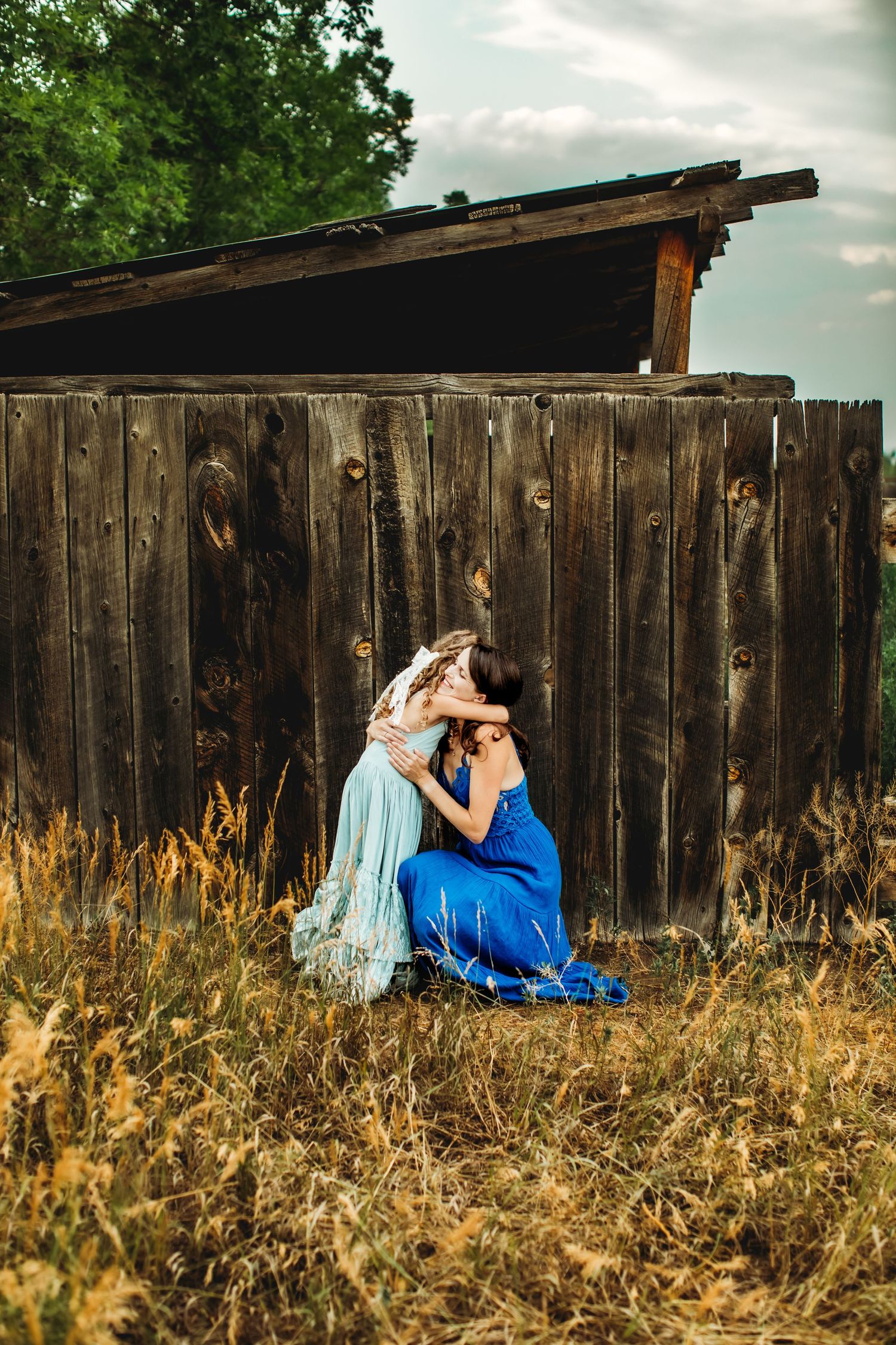 Artistic triptych photo sequence showing couple in blue dress and formal wear sitting against rustic wooden fence at sunset.