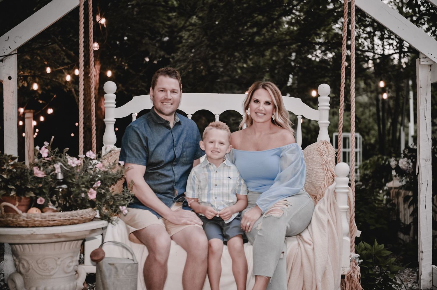 A relaxed family portrait on an elegant white bench with string lights in the background.