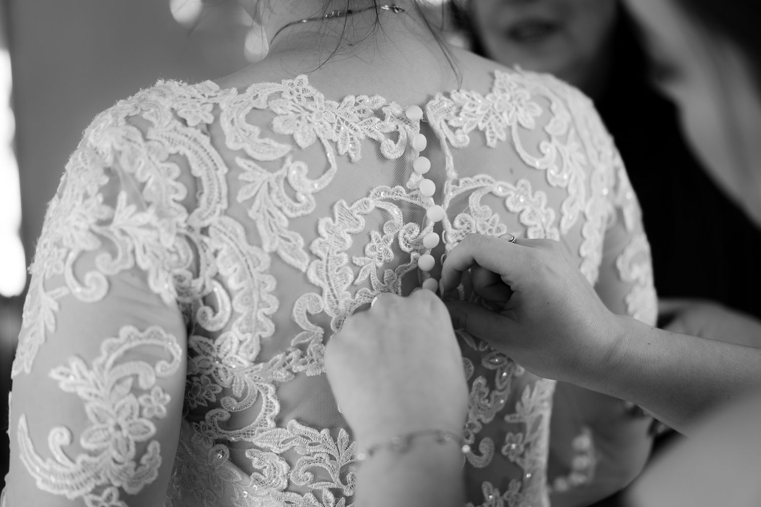 Close-up details of intricate white lace wedding dress being buttoned.