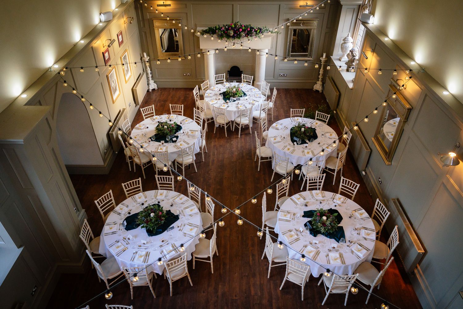Elegant wedding reception setup with round tables and white linens in a warmly lit room. Ellingham Hall