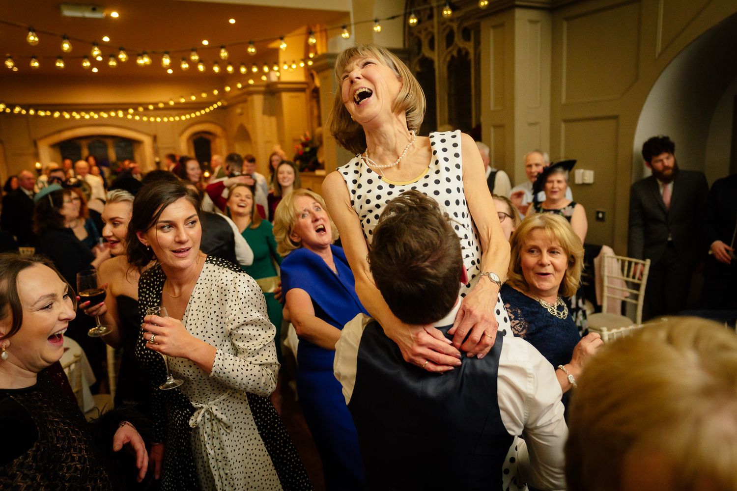 Wedding guests dancing and celebrating at a lively reception with string lights overhead. Ellingham Hall