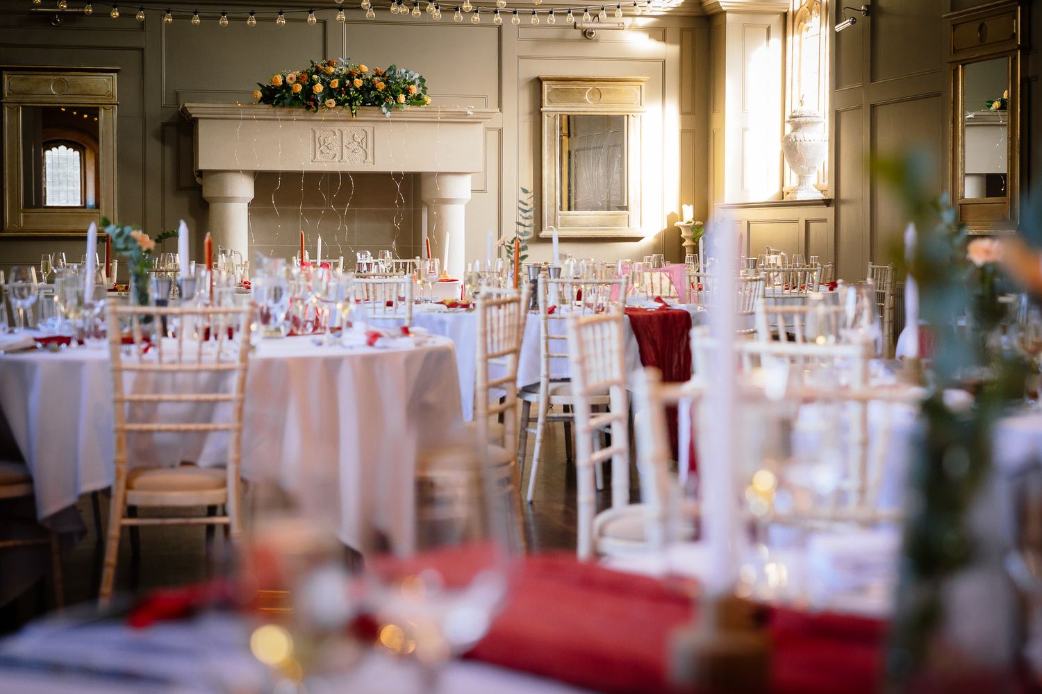 Elegant wedding reception table settings with glassware and red accents.