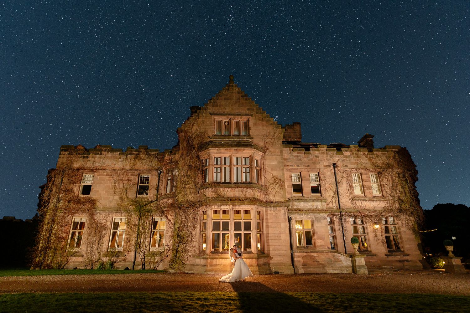 Historic stone mansion illuminated at dusk creates dramatic wedding venue backdrop.