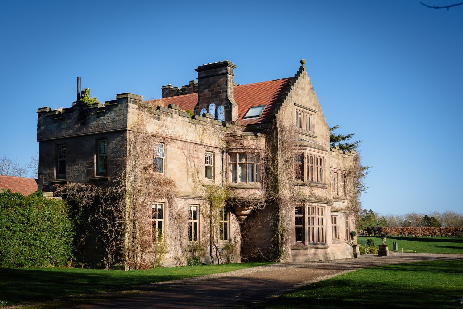Historic stone manor house with red tile roof and ornate architecture photographed against blue sky.