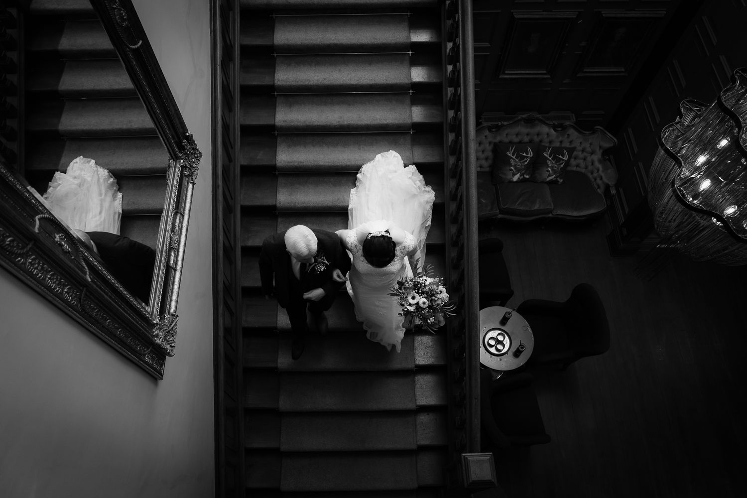 Dramatic black and white overhead view of wedding guests descending a staircase. Ellingham Hall