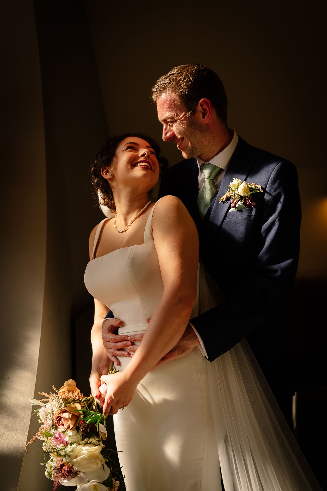 Intimate wedding couple portraits in dramatic lighting with bride in white dress.