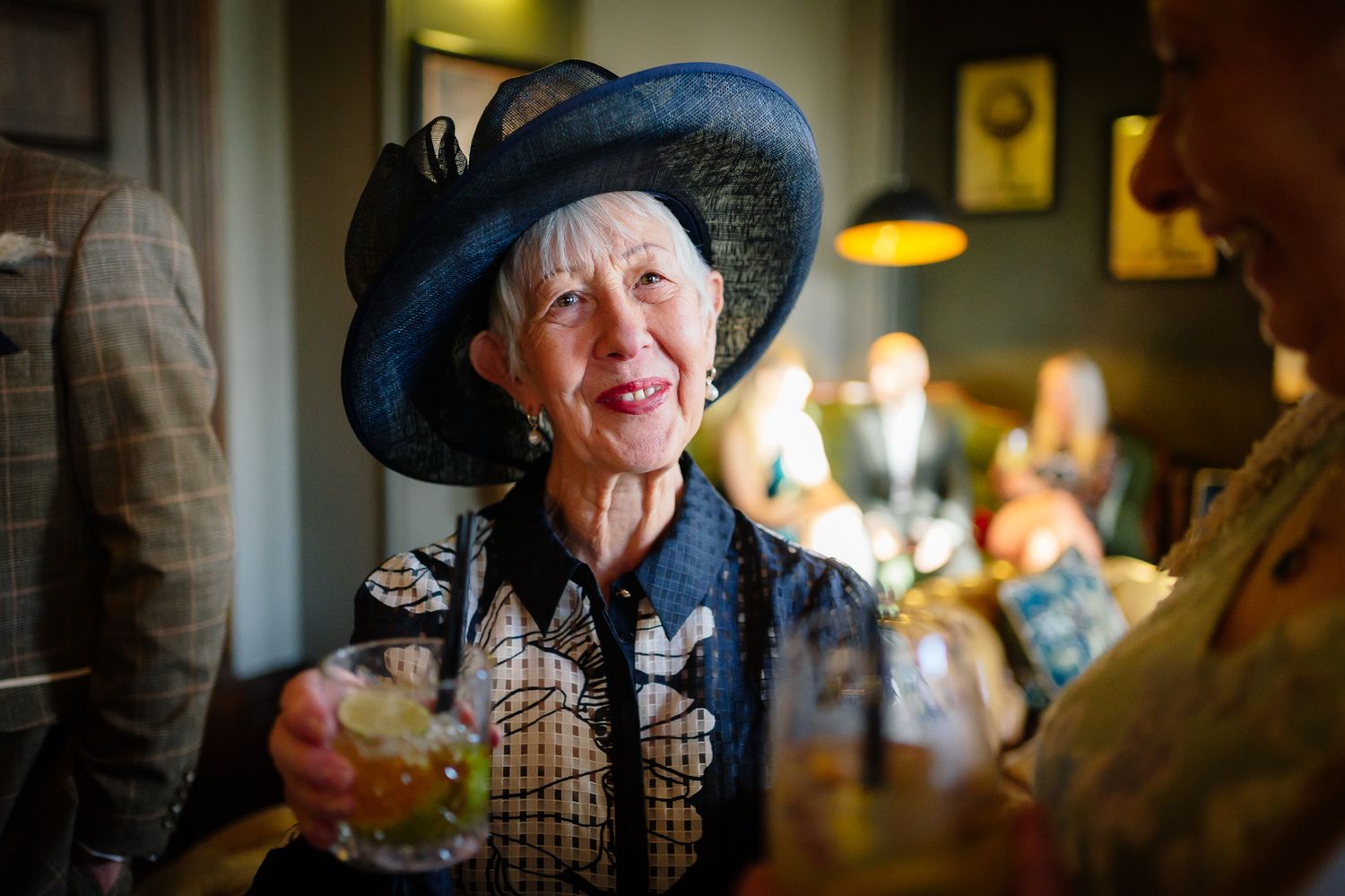 Elegant wedding guest in dark hat enjoying conversation during reception.