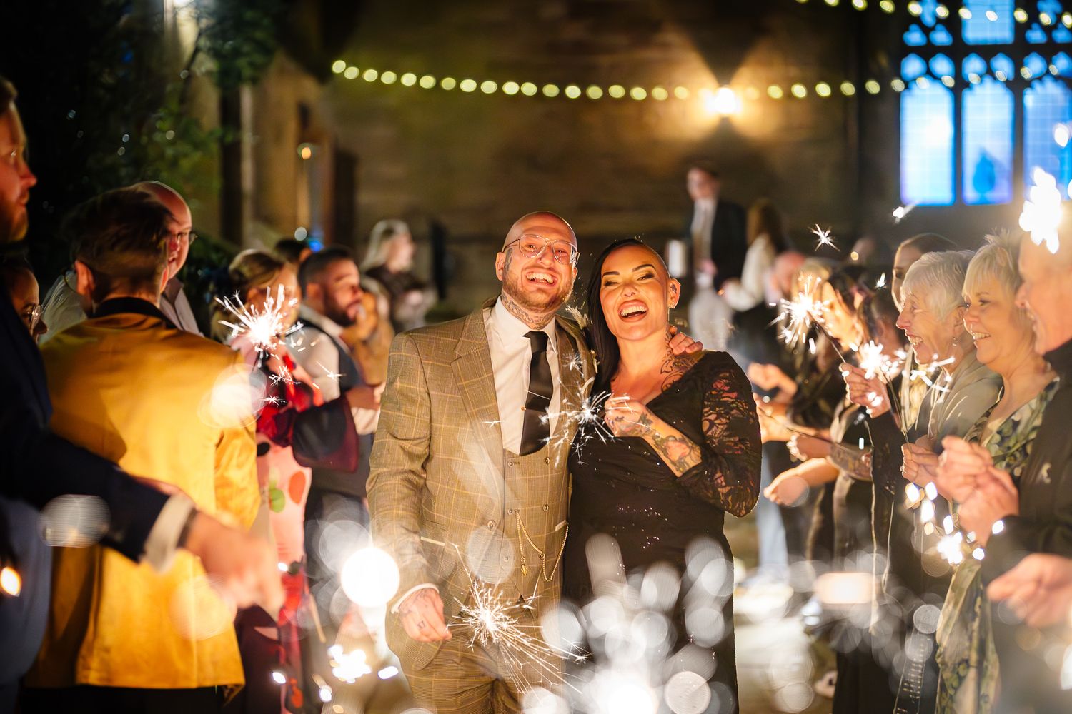 Wedding celebration at night with glowing string lights and sparklers creating magical atmosphere.
