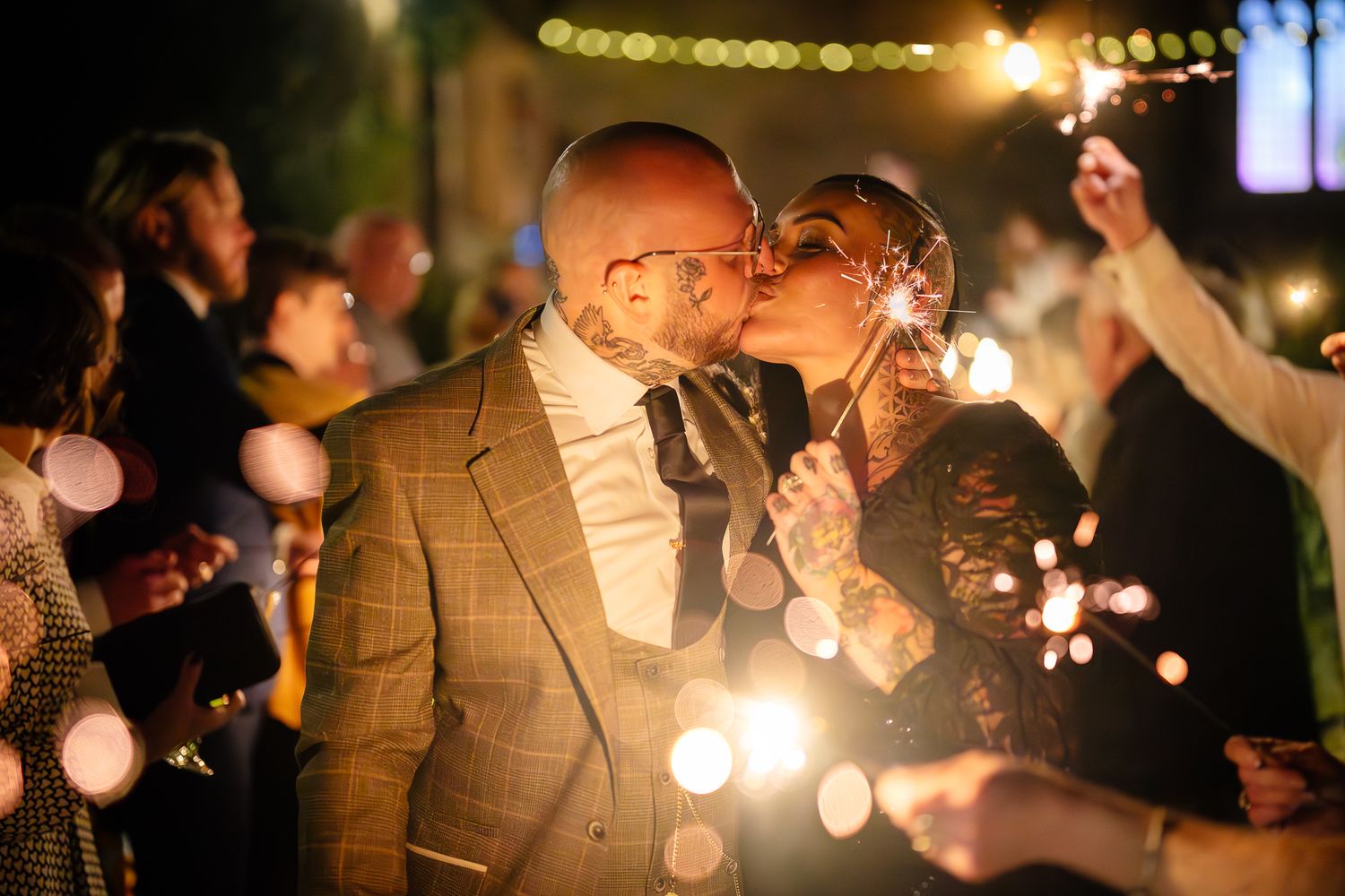Wedding guests dancing and celebrating at an evening reception with glowing string lights overhead.