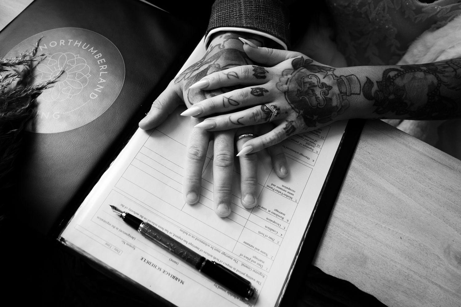Close-up shots of hands signing wedding documents on wooden table.